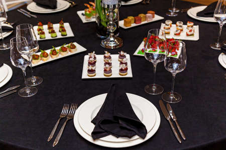 Round table with black tablecloth and black napkins, set of cutlery with snacks for the banquet. Catering, server tables for bonquetの写真素材