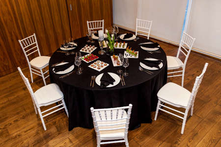 Round table with black tablecloth and black napkins, set of cutlery with snacks for the banquet. Catering, server tables for bonquetの写真素材