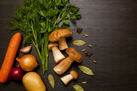 White forest mushrooms on a dark background with vegetables, herbs and spices. Fresh mushrooms on a wooden table.の写真素材