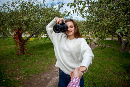 Girl photographer in a white sweater and jeans takes a picture on a professional camera in the park