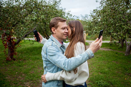 A young couple spends time together in the park, hugging each other and looking at their phones. Guy with a girl with gadgets in the parkの写真素材