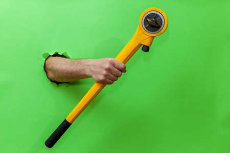 Man holds hand tool for fixing plumbing on green backgroundの写真素材
