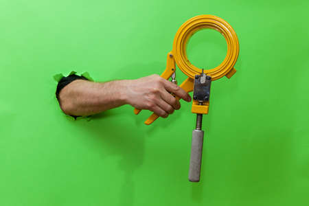 Man holds hand tool for fixing plumbing on green backgroundの写真素材