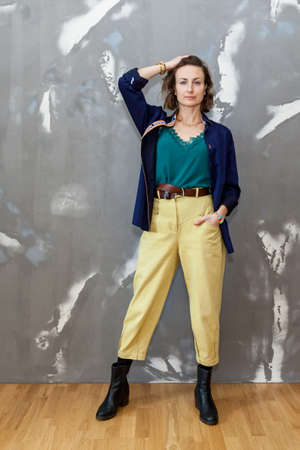 Fashionable and stylish girl posing in yellow trousers, and blouse and a blue shirt against a gray...