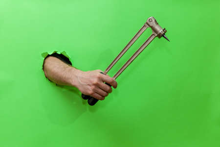 Man holds hand tool for fixing plumbing on green backgroundの写真素材