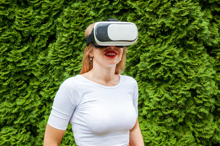 A girl with braces smiles in virtual reality glasses in a park against the backdrop of green trees....