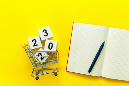Wooden white cubes with the numbers 2023 in a metal trolley and a diary and a pen on a yellow...