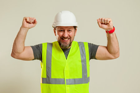A man worker in a vest and a white construction helmet hat shows hand gestures in different poses on a white backgroundの写真素材