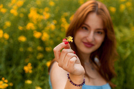 A girl in a blue denim dress holds a yellow rapeseed flower in the fieldの写真素材