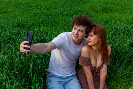 A guy with a girl take a selfie on the phone in green wheat on the field.の写真素材