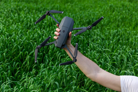 The guy holds a quadrocopter in his hand against the background of young green wheat