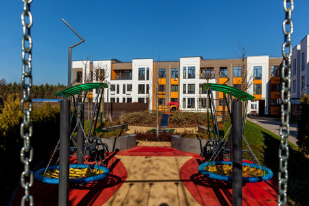 Colorful childrens playground with swings and slide in a safe courtyard surrounded by contemporary apartment buildings under a clear blue skyの写真素材