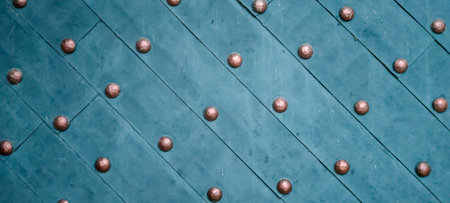 Close-up of a textured diagonal pattern on an aged turquoise metal door adorned with round bronze...