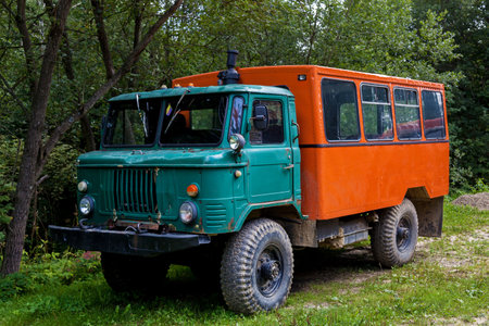 Vintage rugged truck with large tires, green front cabin, and bright orange rear passenger...