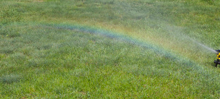 Irrigation system of the lawn at the sunshine produces a rainbow over green grass.の写真素材