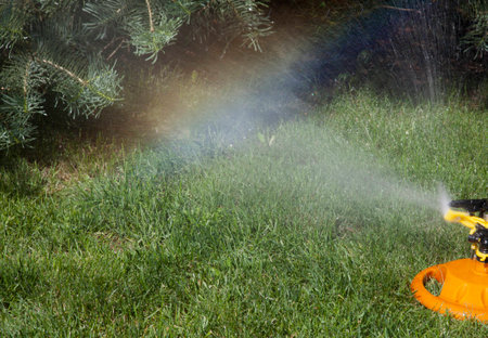Irrigation system of the lawn at the sunshine produces a rainbow over green grass.の写真素材