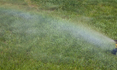 Irrigation system of the lawn at the sunshine produces a rainbow over green grass.の写真素材