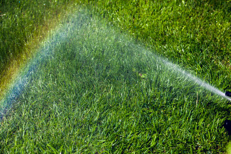 Irrigation system of the lawn at the sunshine produces a rainbow over green grass.の写真素材