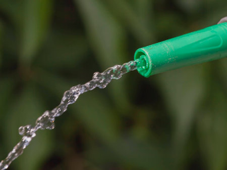 Jet of water rises from the tip of device of irrigation of garden at the sunshine on background of green plants.の写真素材