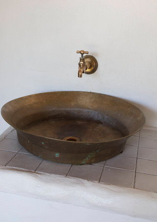 On the white wall the old brass faucet and sink on top at white tiles in the gazebo in the garden.の写真素材