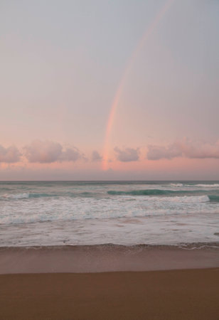 Rainbow, pink colors of clouds and sea foam on waves. Big surf waves.の写真素材
