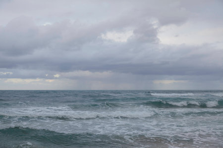 Thunderstorm under sea and waves, white clouds and sea foam, dark yellow sand beach.の写真素材