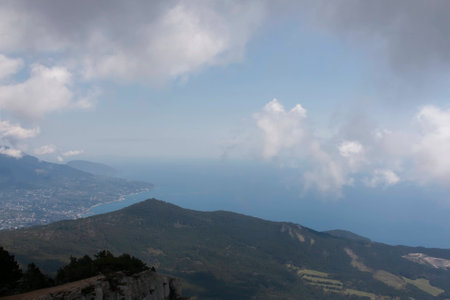 Sunny summer day. The sea merges with the sky on the horizon. Clouds close. Green hills and small town on the shore. Ukraine, Crimea.の写真素材