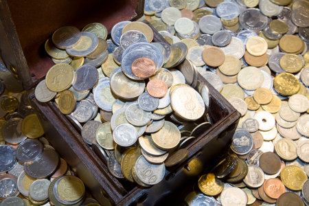 Chest with coins of different countries. Around as many coins scattered.の写真素材