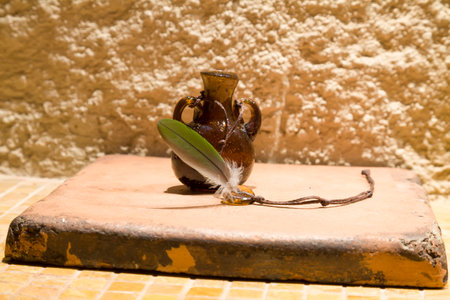 Jar of dark glass on the background of a concrete wall. Vintage bank. Extremely light. Feather bird with blue, green and gray color. Bead glass on a shoestring.の写真素材