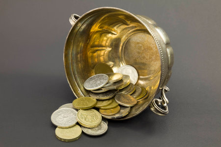 Natural antique old bowl made of silver lying on its side with coins on a dark background.の写真素材