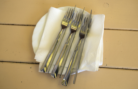on a wooden table a plate. On the plate are cutlery forks and knives.の写真素材
