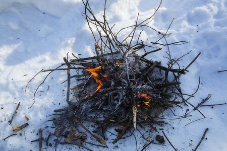 A bonfire on the snow in the winter. thin branches in the flame of fire.の写真素材