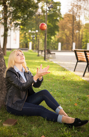 beautiful blond girl catches an apple near the treeの写真素材