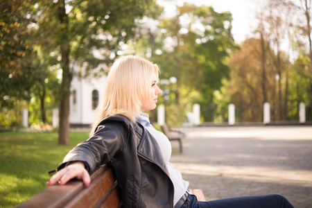 beautiful blond girl sitting on a bench and looking aheadの写真素材