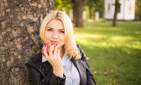 beautiful blond girl holding an apple near the treeの写真素材