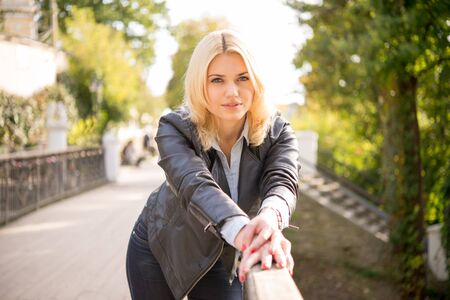 pretty blond girl standing on the bridge leaning on railingの写真素材