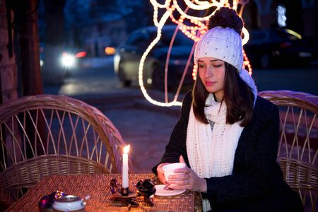beautiful girl sitting outdoors in winter with a cup and a candleの写真素材
