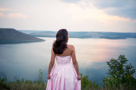 beautiful girl in a dress looks at the horizon of the riverの写真素材