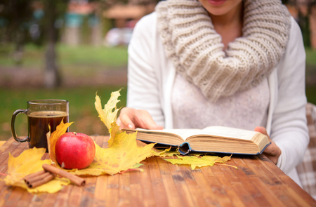 girl reading a book at the table with autumn leavesの写真素材