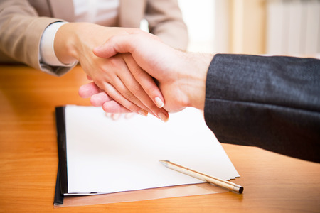 Handshake of a woman's and a man's hand near the documentの写真素材