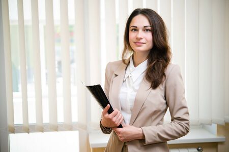 Young business woman stands with a folder near the window in the office