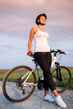 relaxed pretty athletic girl with a bicycle at sunsetの写真素材