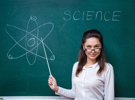 Young teacher with glasses talks about science near blackboardの写真素材