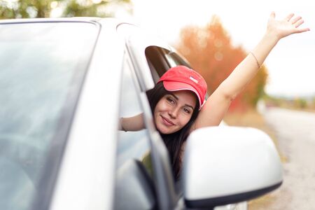Pretty girl in a cap waving her hand while drivingの写真素材