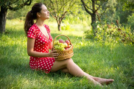 young pretty girl sitting in the garden holding a basket of fruit on her kneesの写真素材