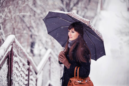 Beautiful young woman with umbrella in snowfall toned imageの写真素材