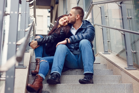 Beautiful young couple in love on a date outdoors on modern urban background. Smiling and hugging. Bearded handsome man and brunette pretty woman in casual dress.の写真素材