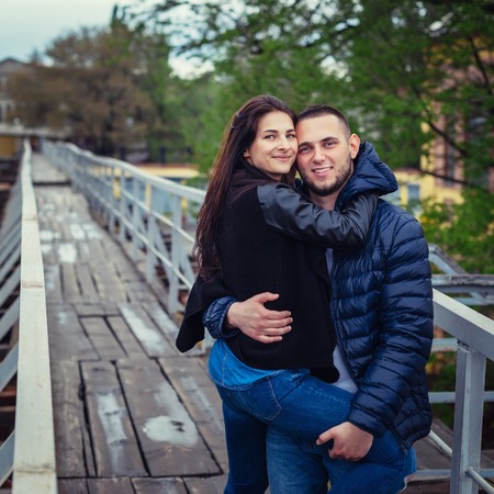 Beautiful young couple in love on a date outdoors on modern urban background. Smiling and hugging. Bearded handsome rustic man and brunette pretty woman in casual dress.の写真素材
