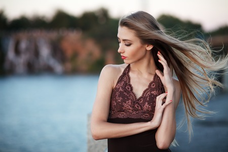 Beautiful young fashionable woman posing in dress at the river coast in the evening after sunset. Vogue style. Urban backgroundの写真素材