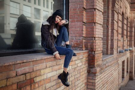 Outdoor lifestyle portrait of pretty young girl, wearing hipster swag grunge style on urban background. Wearing hat and jeans with backpack. Spring fashion woman.の写真素材